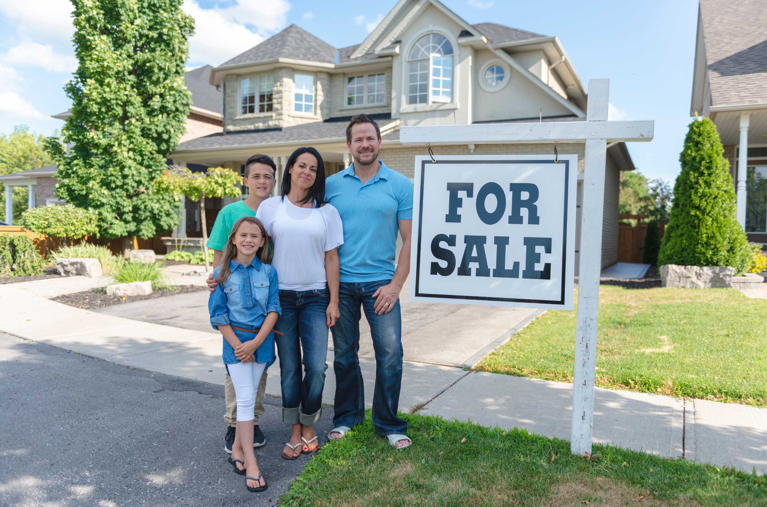 Family standing in front of a 'For Sale' sign.